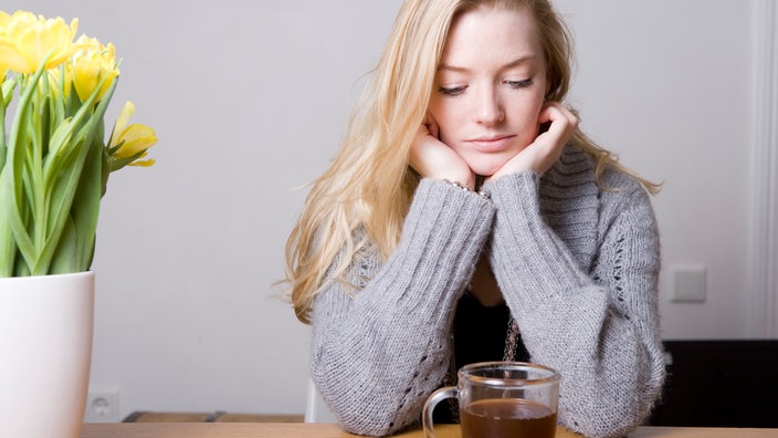 Eine junge Frau sitzt am Tisch und schaut traurig auf ihre Teetasse. | Bildquelle: dpa/picture-alliance/Selina Pfrüne Eine junge Frau sitzt am Tisch und schaut traurig auf ihre Teetasse.